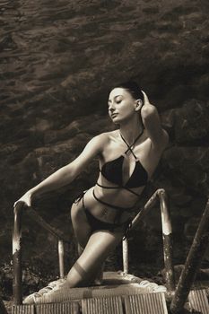 Adult woman in a strappy bikini posing by water, exuding confidence.