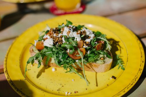 Free A vibrant and healthy avocado toast topped with cherry tomatoes, arugula, and feta cheese on a yellow plate. Stock Photo