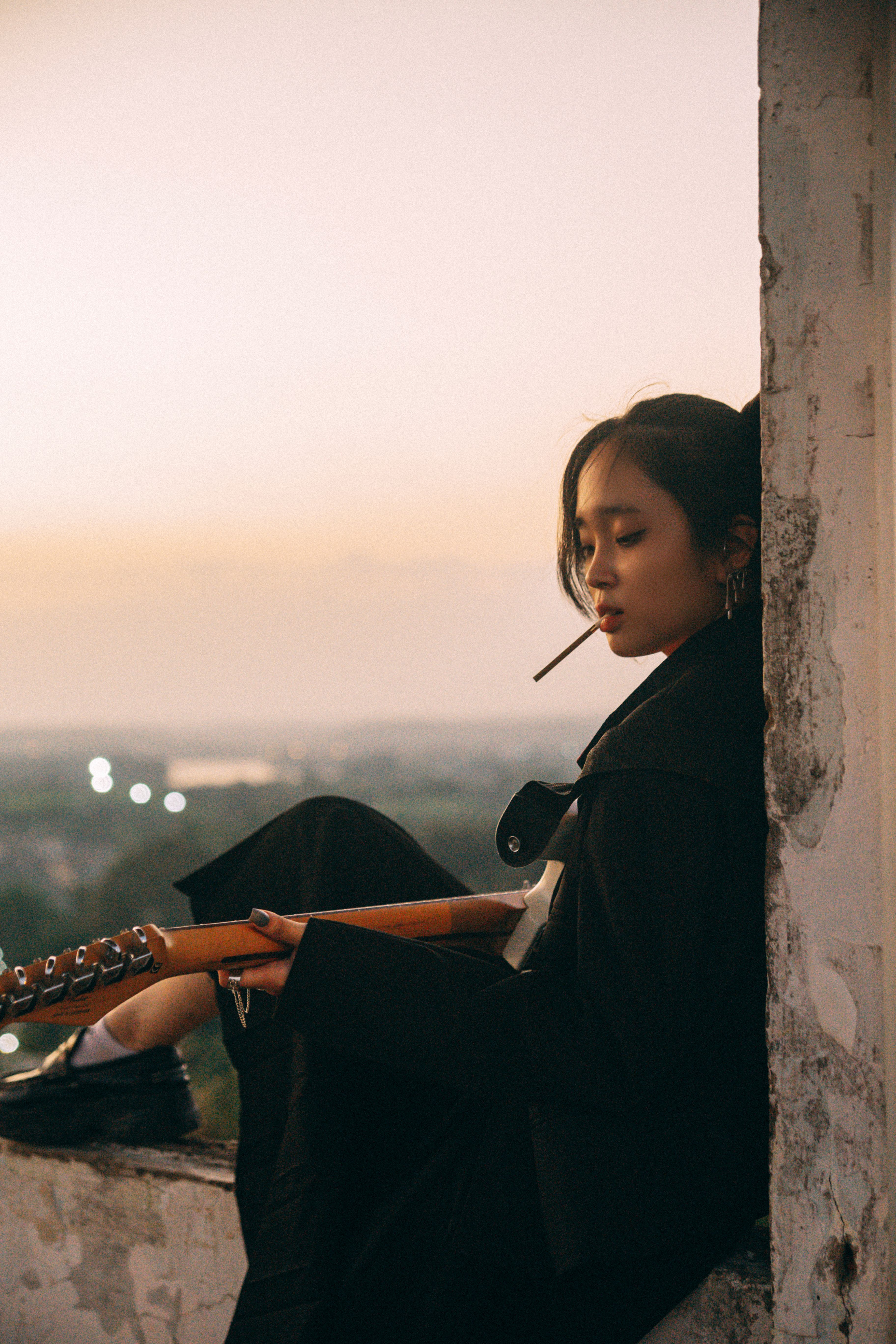 A young woman with a guitar relaxes on a rooftop during sunset, exuding a serene and contemplative mood.