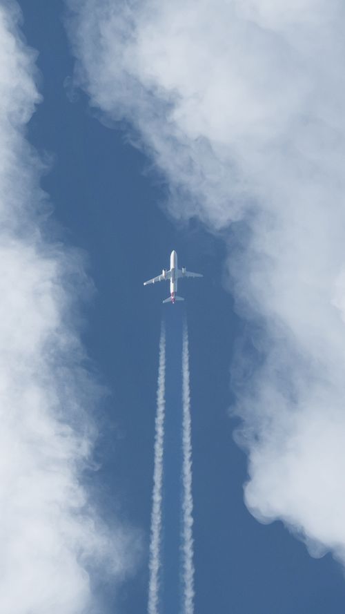 Free A jet airliner soaring high in the sky with visible contrails and surrounding clouds. Stock Photo
