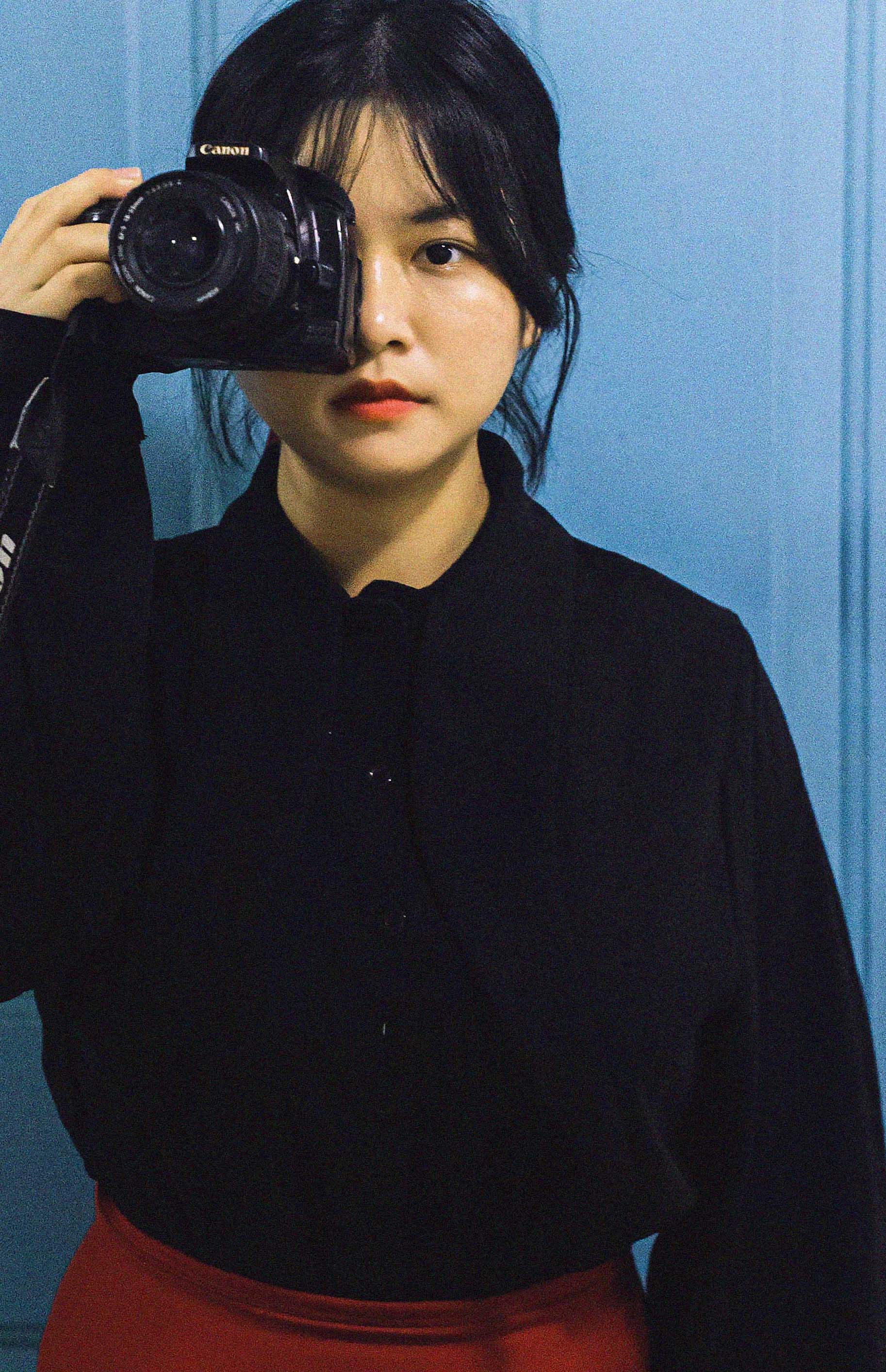 Woman in black attire holding a camera against a blue background.