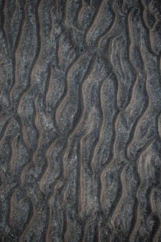 Close-up of intricate dark sand textures creating a natural abstract pattern.