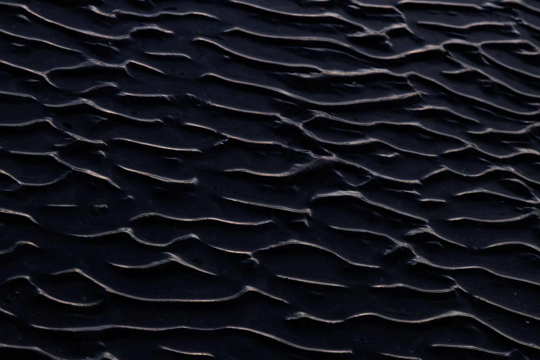 Close-up view of dark sand ripples creating a unique abstract texture pattern.