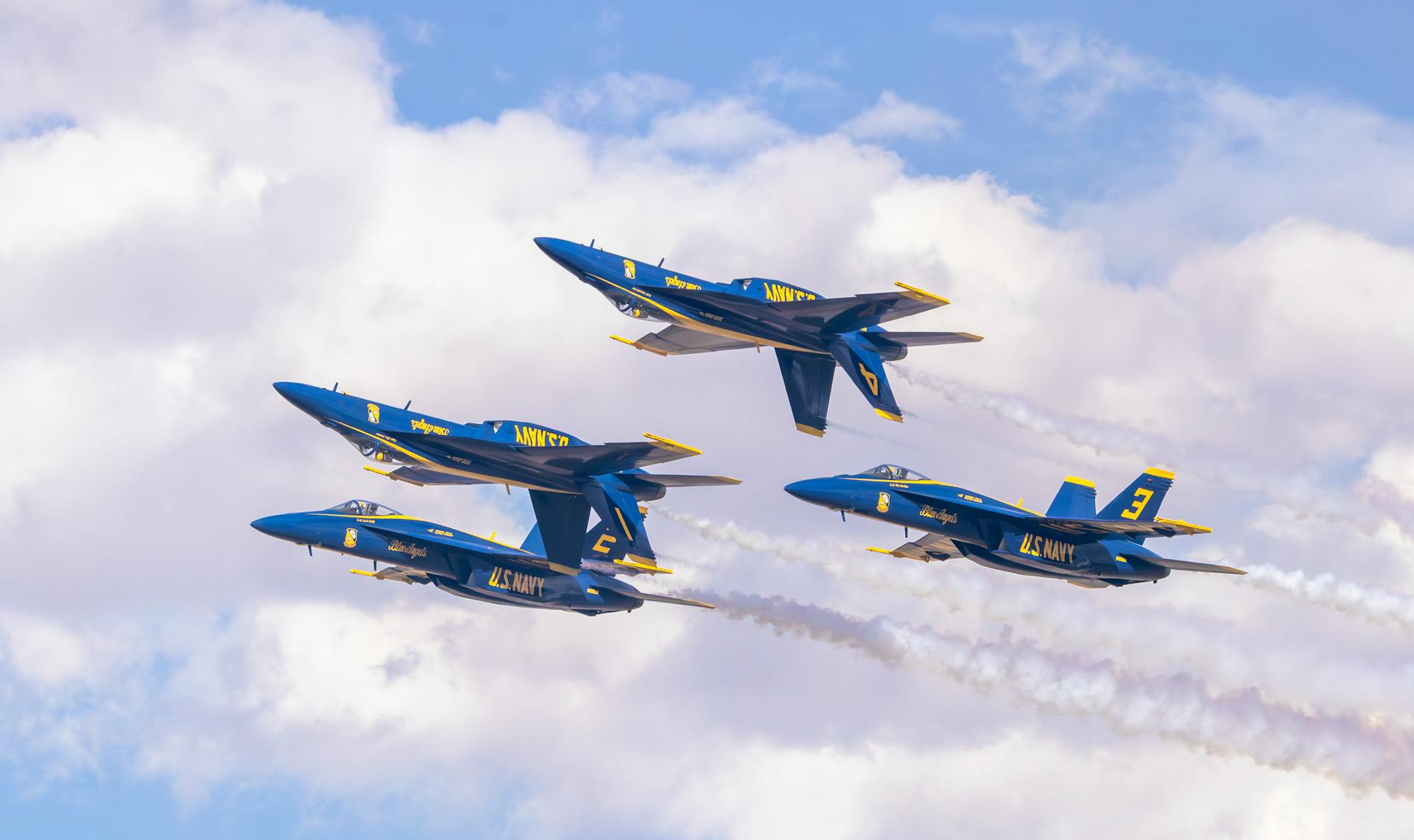 US Navy Blue Angels jets in precise aerobatic formation against a clear sky.