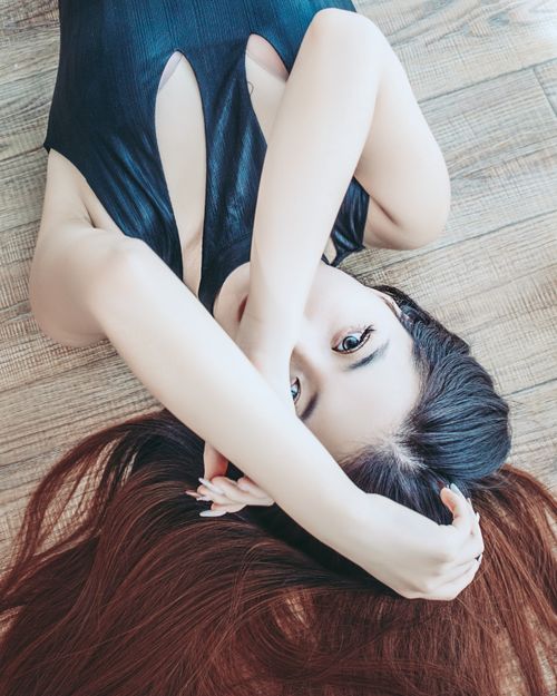 Free Artistic pose of a woman in a black dress lying on a wooden floor. Stock Photo