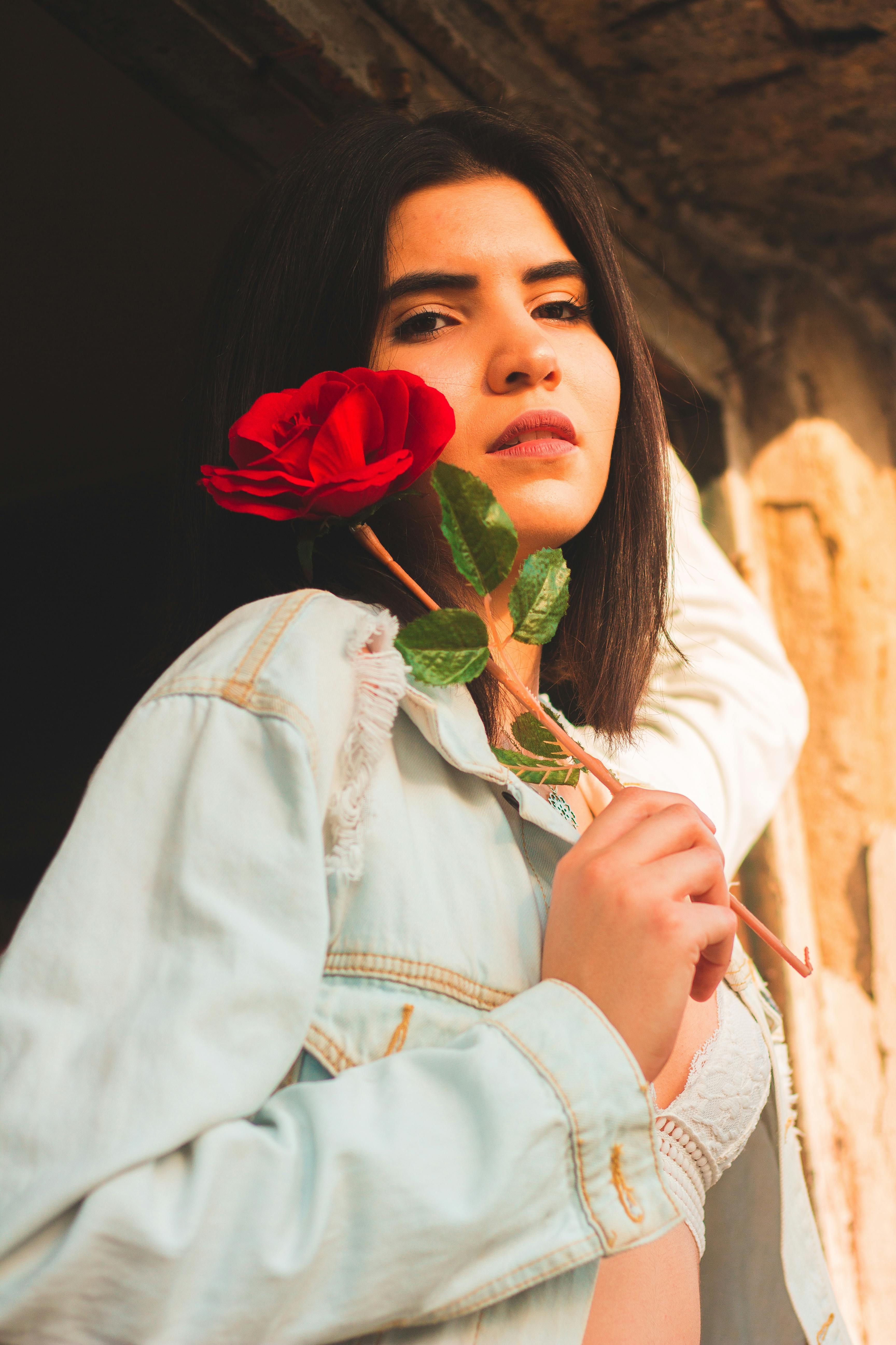 在温暖的自然灯光下，一位黑发女子的肖像中，长着一朵红玫瑰