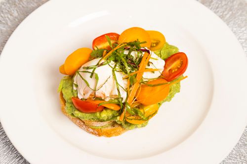 Free Colorful avocado toast with poached egg, cherry tomatoes, and garnishes on a white plate. Stock Photo