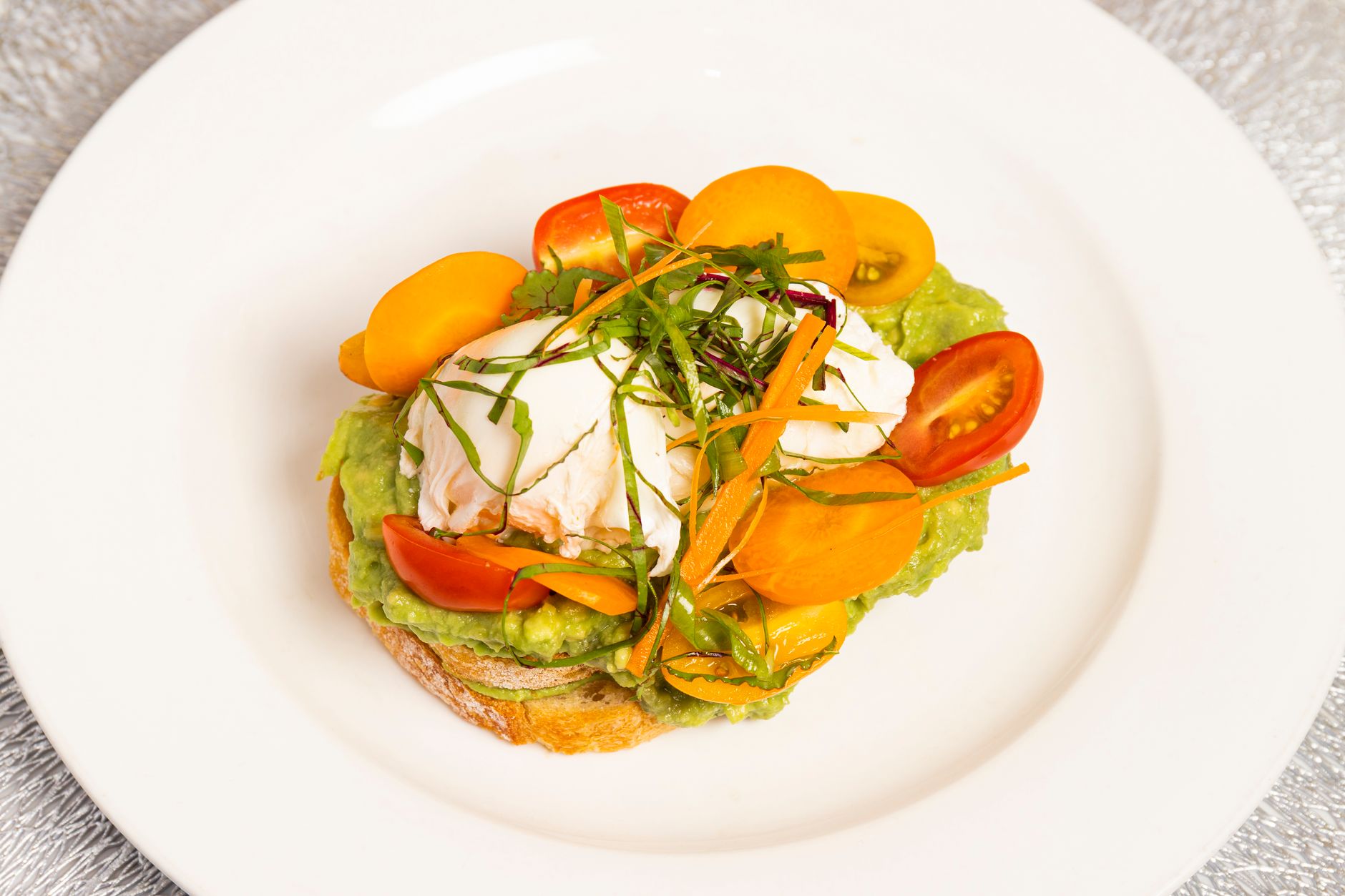 Delicious poached egg on avocado toast with cherry tomatoes and herbs, served in a gourmet style.