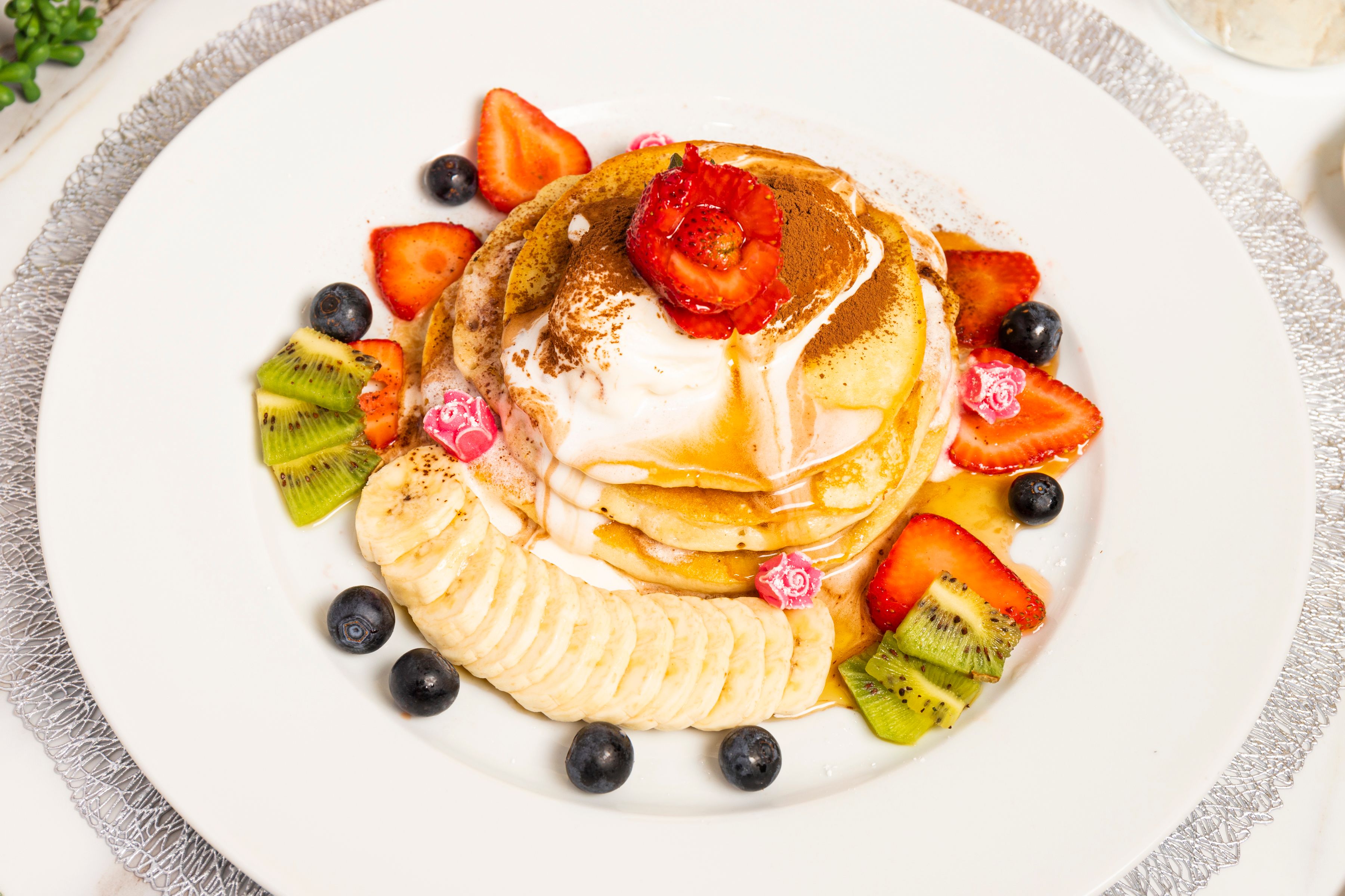 Delicious stack of pancakes topped with fresh fruits, whipped cream, and syrup for a gourmet breakfast.