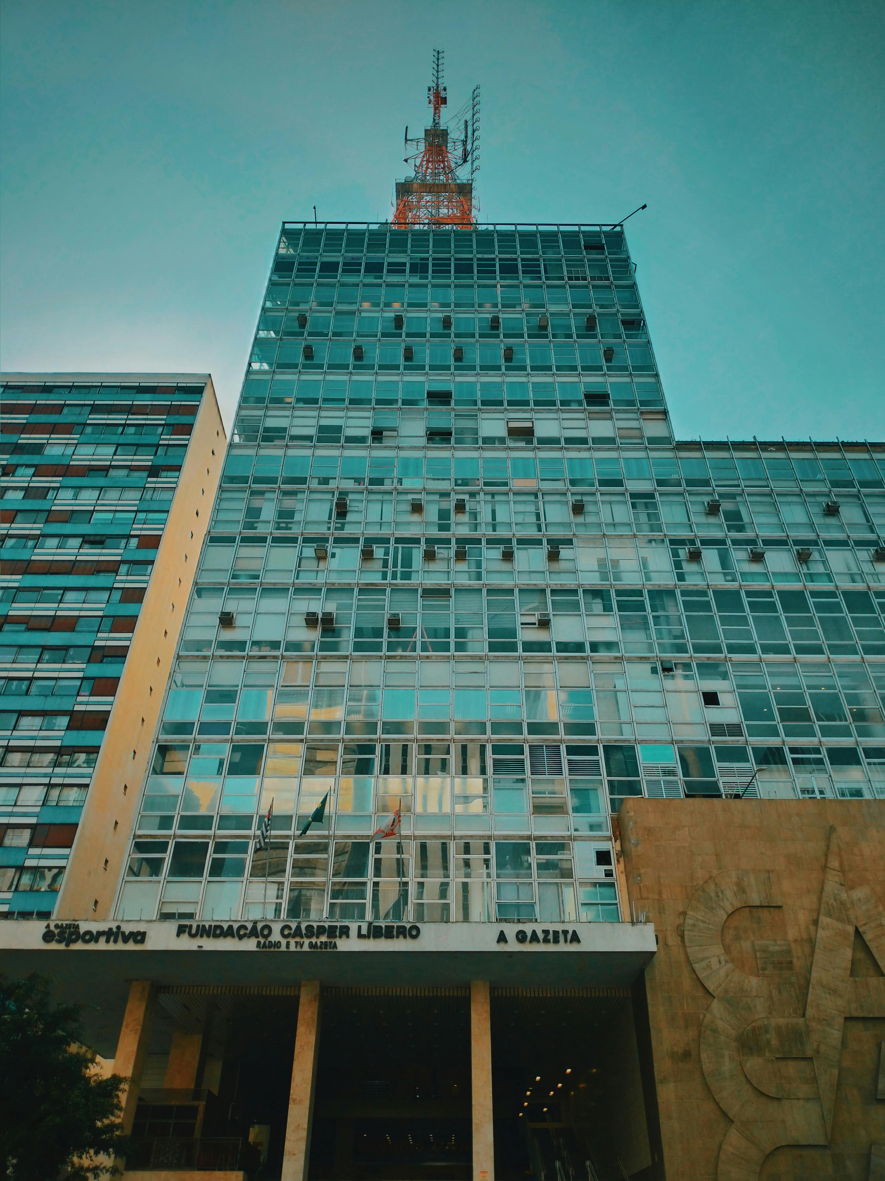 晴朗蓝天下，现代摩天大楼的玻璃立面和可见天线呈现低角度视图