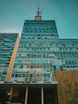 晴朗蓝天下，现代摩天大楼的玻璃立面和可见天线呈现低角度视图