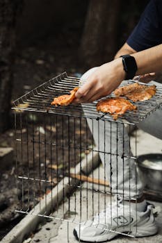 Person grilling seasoned chicken on barbecue grill outside in casual setting.