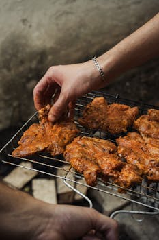 Close-up of hands placing marinated chicken on a grill for a barbecue.