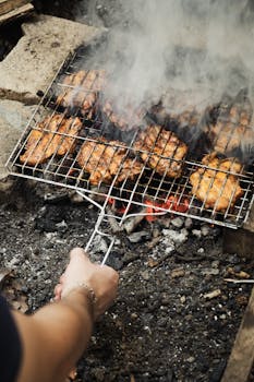 Close-up of marinated chicken being grilled over open charcoal fire outdoors.