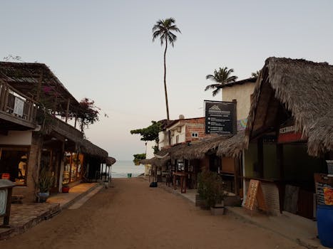 Tranquil street scene in Jericoacoara, Brazil, featuring palm-lined shops and thatched roofs at dusk.