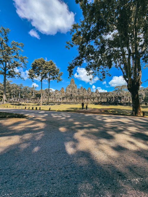 Free Stunning view of Angkor Wat among tall trees with clear blue sky and few visitors present. Stock Photo
