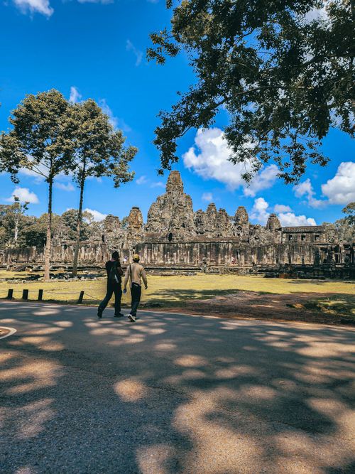 Free Tourists walk near the historic ruins of Angkor Wat in Cambodia under clear blue skies. Stock Photo