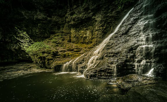 A tranquil waterfall flowing over moss-covered rocks in a lush outdoor setting.