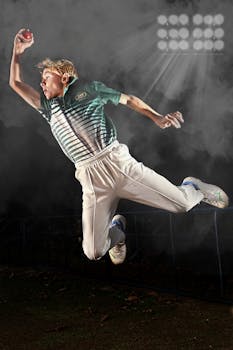 An energetic cricketer leaps to catch a cricket ball under stadium lights.