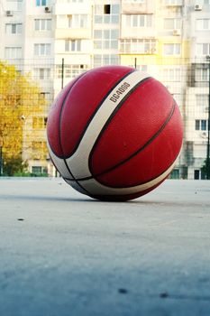 Red basketball resting on a concrete court in a city neighborhood with apartment buildings.