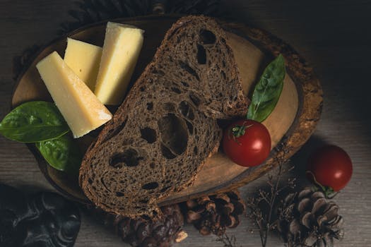 A dark rustic bread with cheese wedges, cherry tomatoes, and basil on a wooden board.