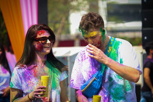Two people enjoy the vibrant Holi festival in Jaipur, covered in colorful powders.