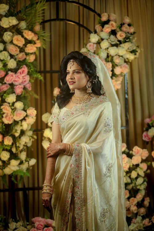 Free Bride in cream saree with henna, surrounded by flowers, exuding timeless elegance. Stock Photo