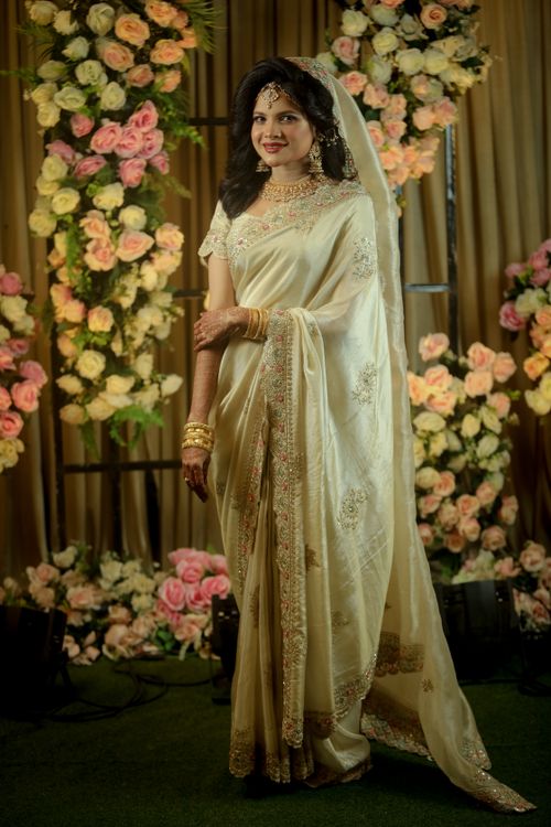Free A bride in a beautiful saree posing indoors with floral decorations at a wedding. Stock Photo