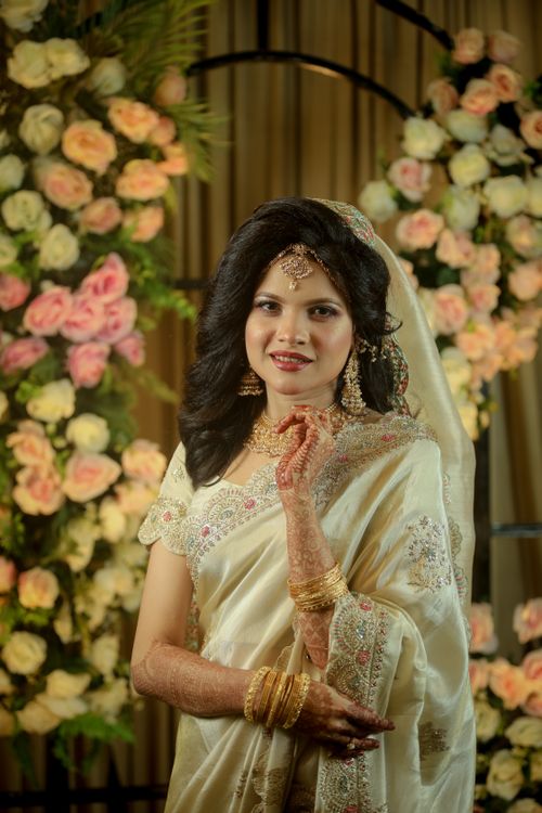 Free A beautiful bride in a traditional saree poses with a floral backdrop, exuding grace. Stock Photo