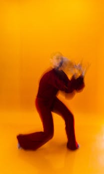 A contemporary dancer creates motion blur against a vivid orange backdrop in a studio.