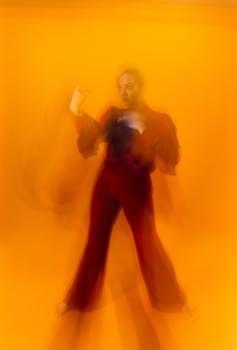 Artistic image of a contemporary dancer with motion blur on an orange backdrop, showcasing movement and energy.