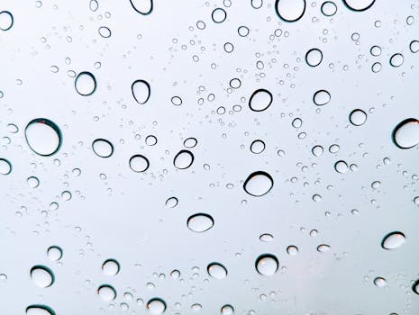 Close-up of raindrops on glass with abstract patterns and reflections.