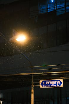 Street lamp illuminating Charoen Krung Road sign on a rainy night.