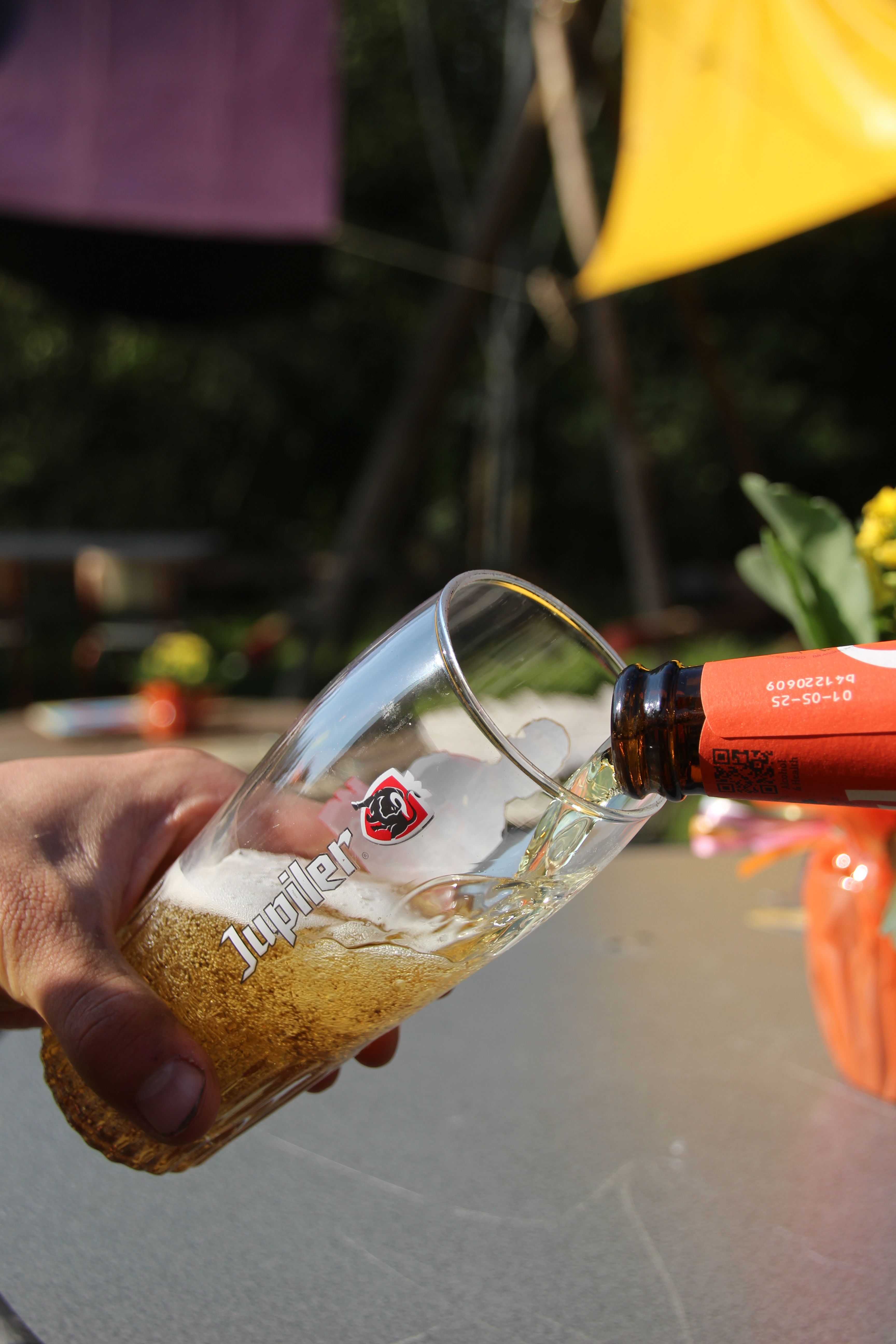 Close-up of beer being poured into a glass outdoors on a sunny day.