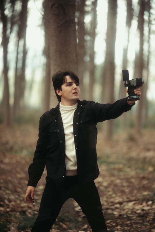 Free Man capturing outdoor scenes with a camera in a wooded area. Creative filming concept. Stock Photo