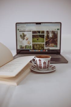 A cozy setup with coffee, an open book, and a laptop screen displaying nature images.