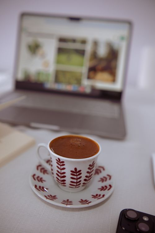 Free Cup of coffee on a desk with a laptop screen in the background. Stock Photo