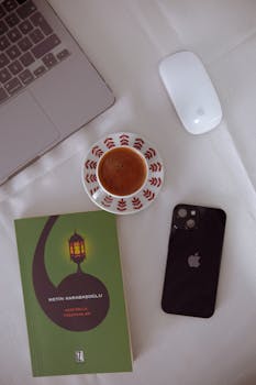Cozy flat lay featuring coffee, book, phone, and laptop on a white tablecloth.