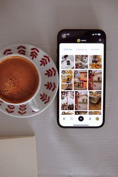 Top view of smartphone with social media app next to a coffee cup on a table.