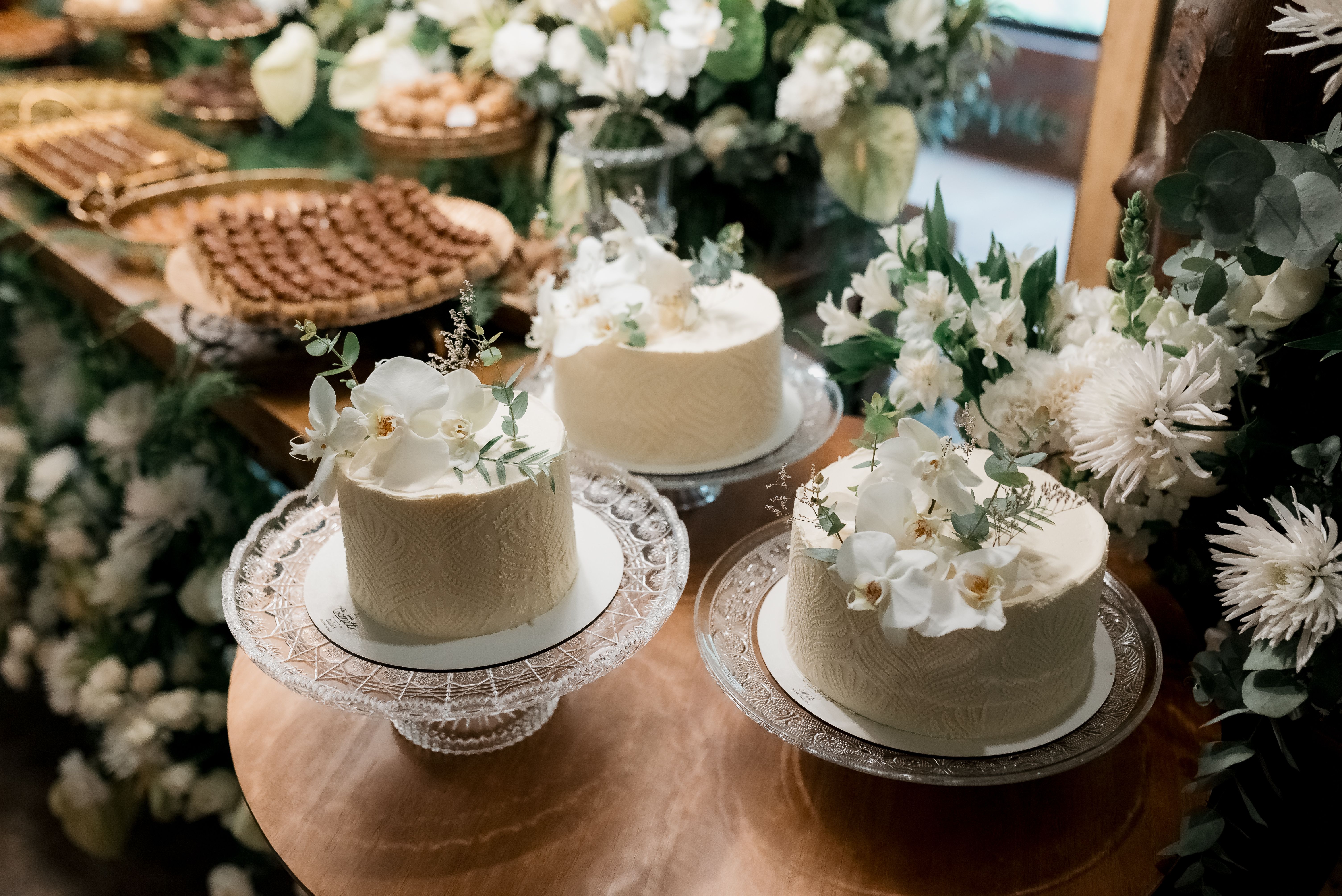 Beautifully decorated wedding cakes with floral accents surrounded by lush greenery.