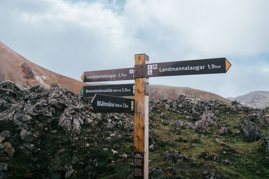 Trail signposts in Landmannalaugar, Icelandic Highlands with rocky terrain and colorful mountains.