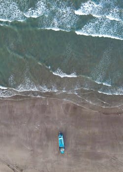 Stunning aerial shot of a blue boat on Muscat's coastal beach with turquoise waves.