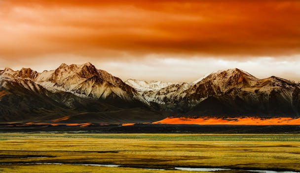Scenic view of snow-capped mountains under a vibrant orange sky during sunset.