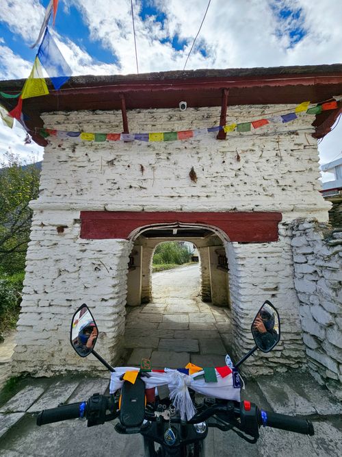 Free Motorbike passing through a historic whitewashed gateway in Nepal adorned with colorful prayer flags. Stock Photo