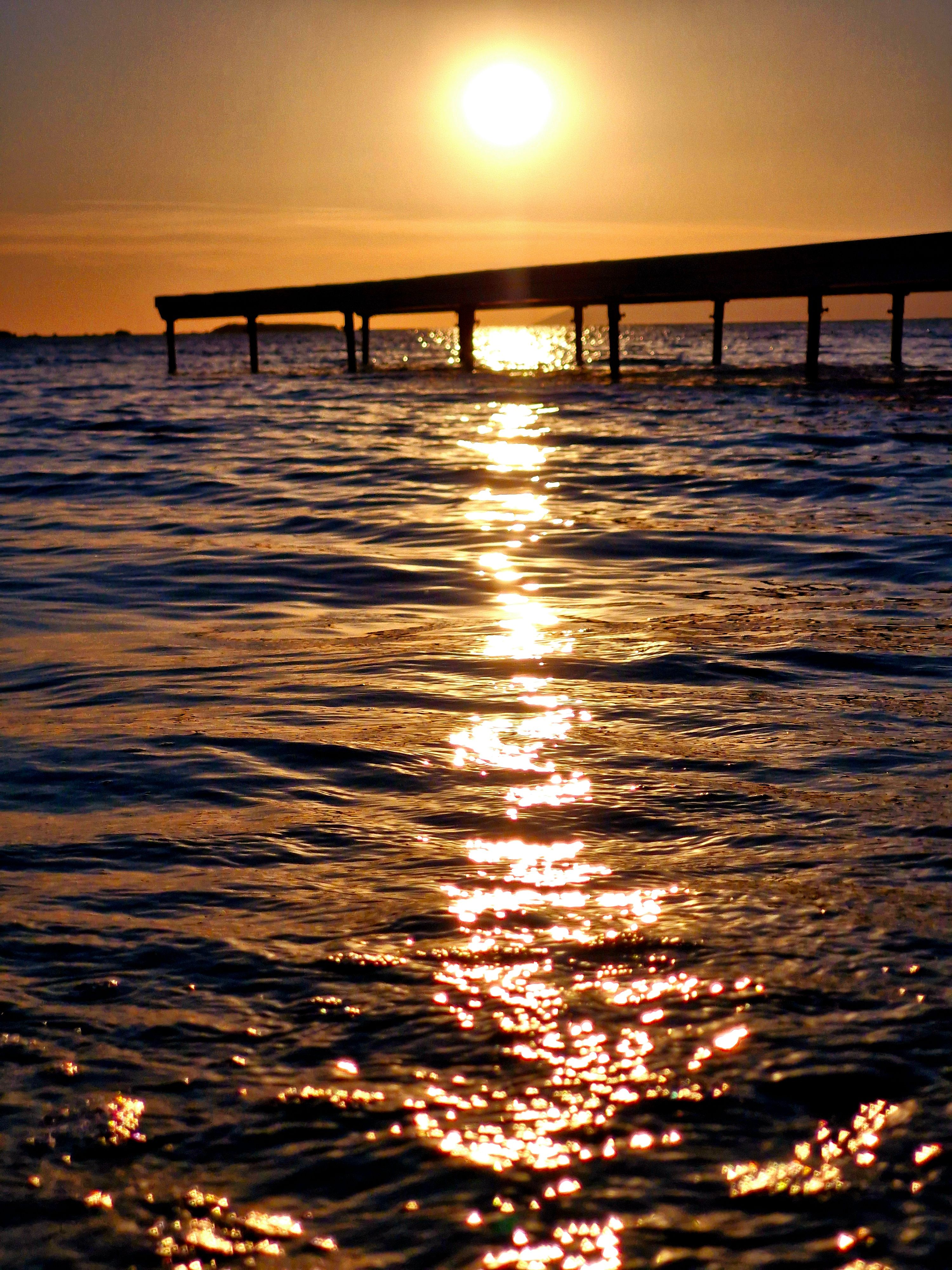 Sunset over tranquil ocean with pier silhouette · Free Stock Photo