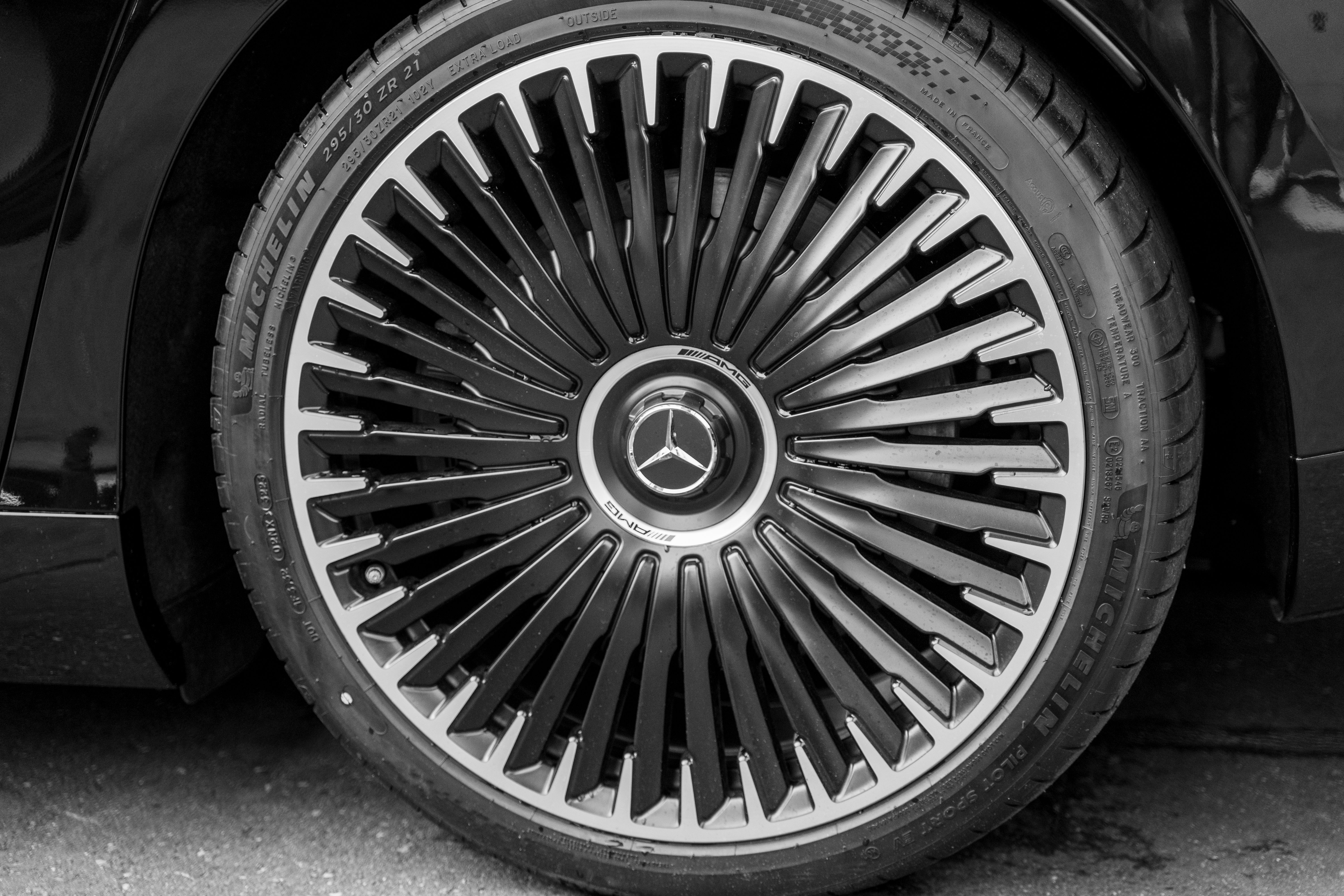 Black and white image of a high-end car wheel rim with intricate design.