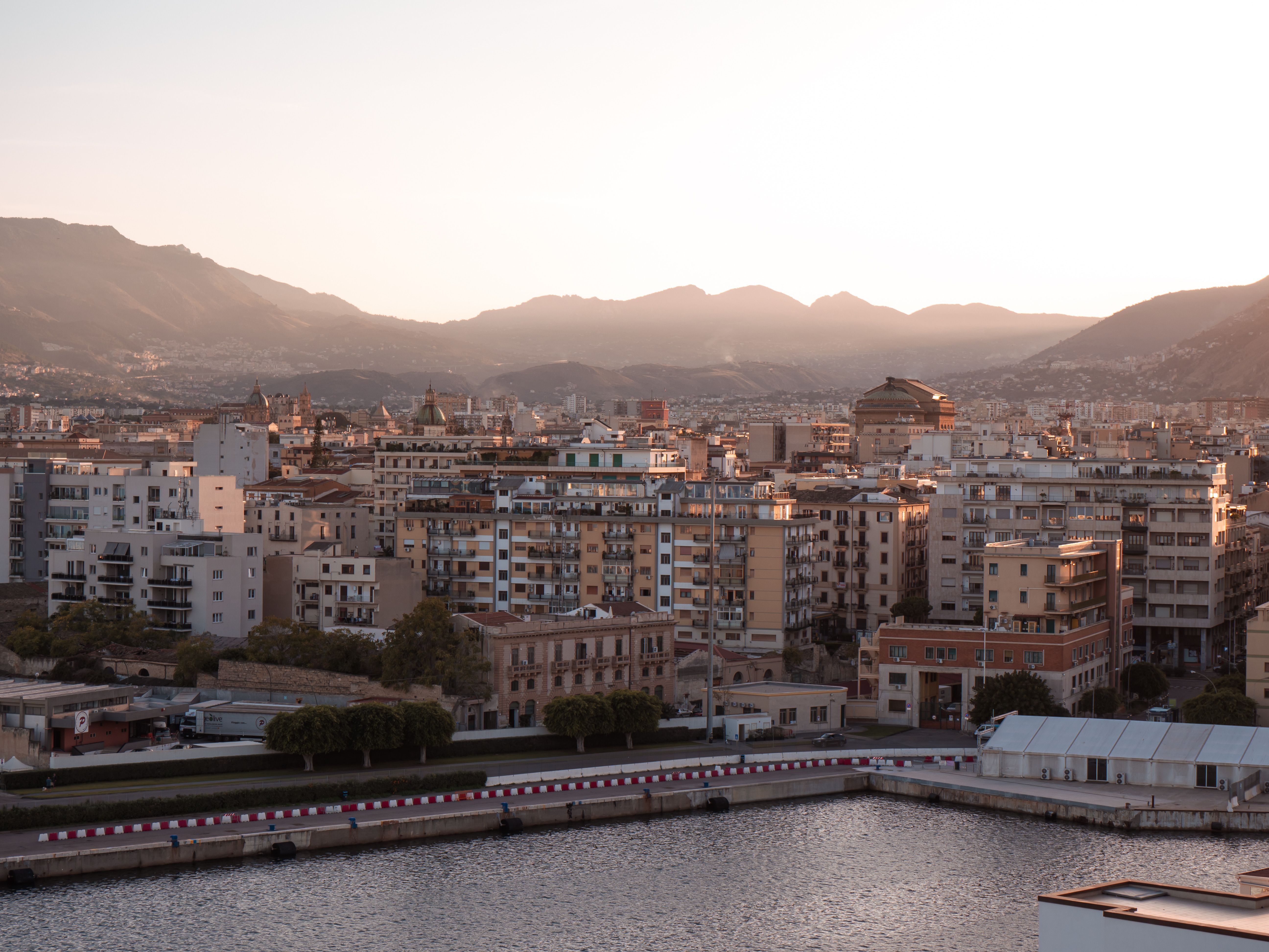 A picturesque view of Palermo, Sicily, with mountains and buildings at sunset.