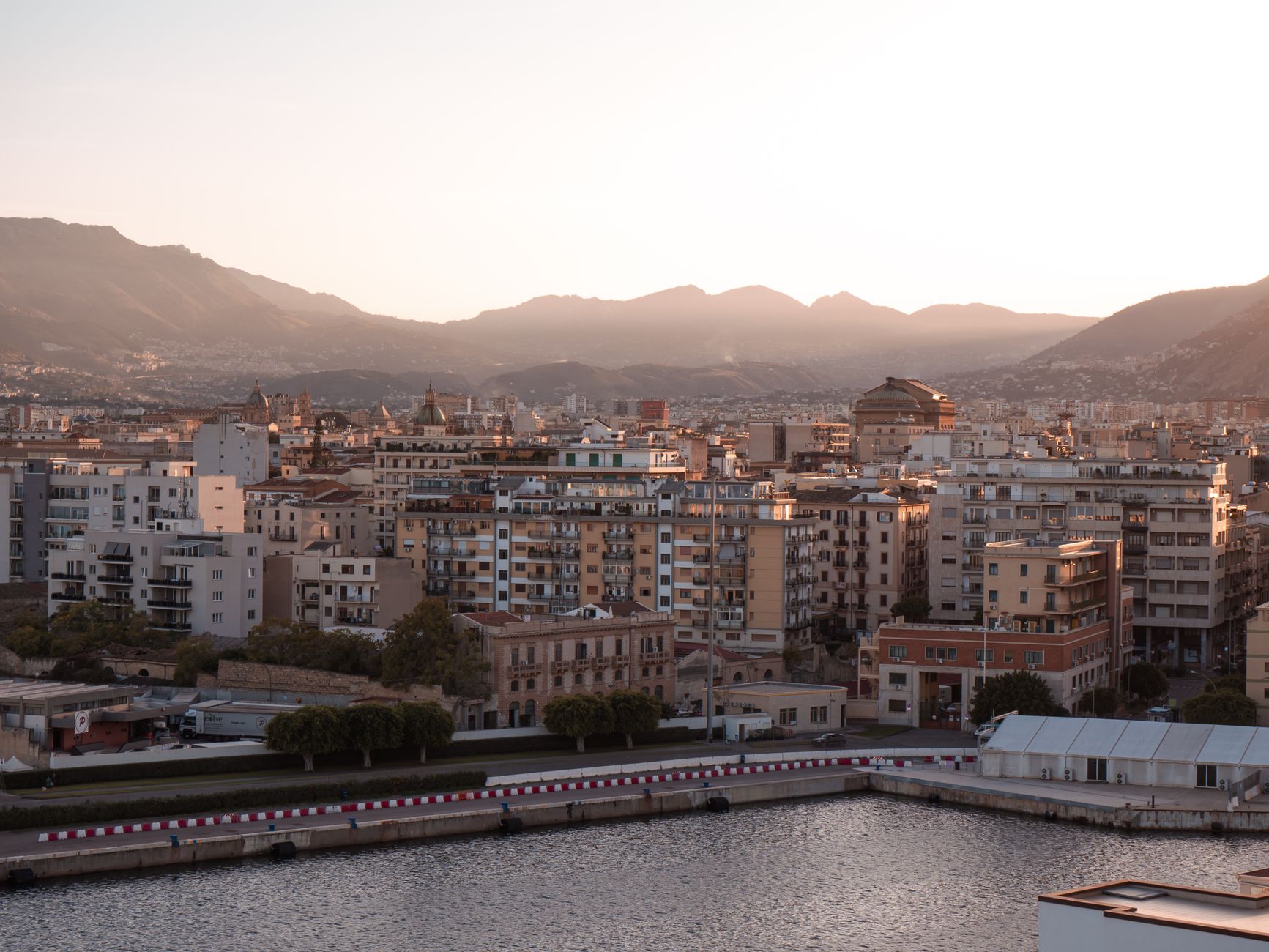 A picturesque view of Palermo, Sicily, with mountains and buildings at sunset.