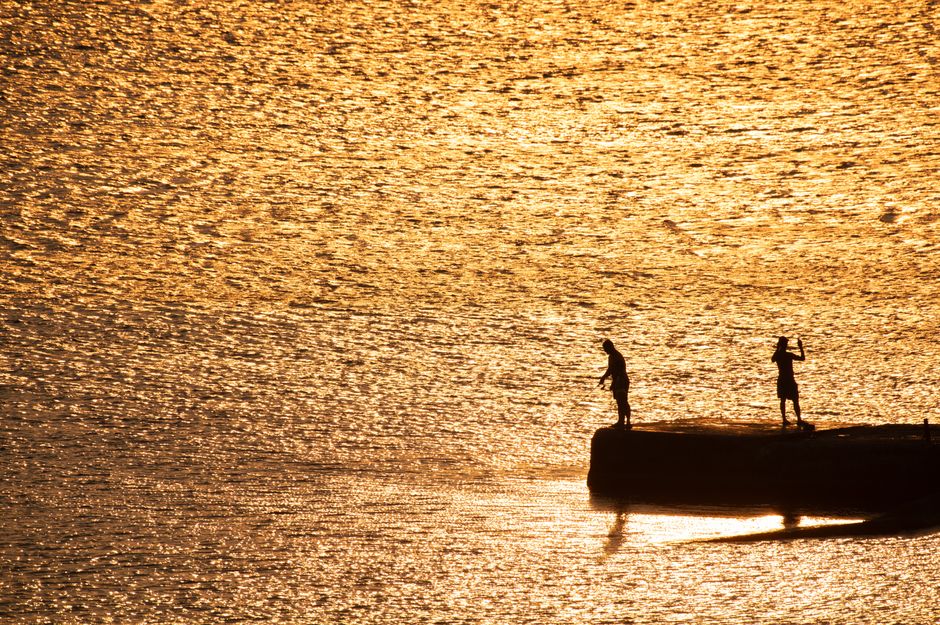 Silhouettes of two people at sunset, against a shimmering golden sea backdrop.