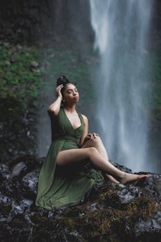 一位身着绿裙的优雅女子，在瀑布旁摆着姿势，散发着宁静与优雅